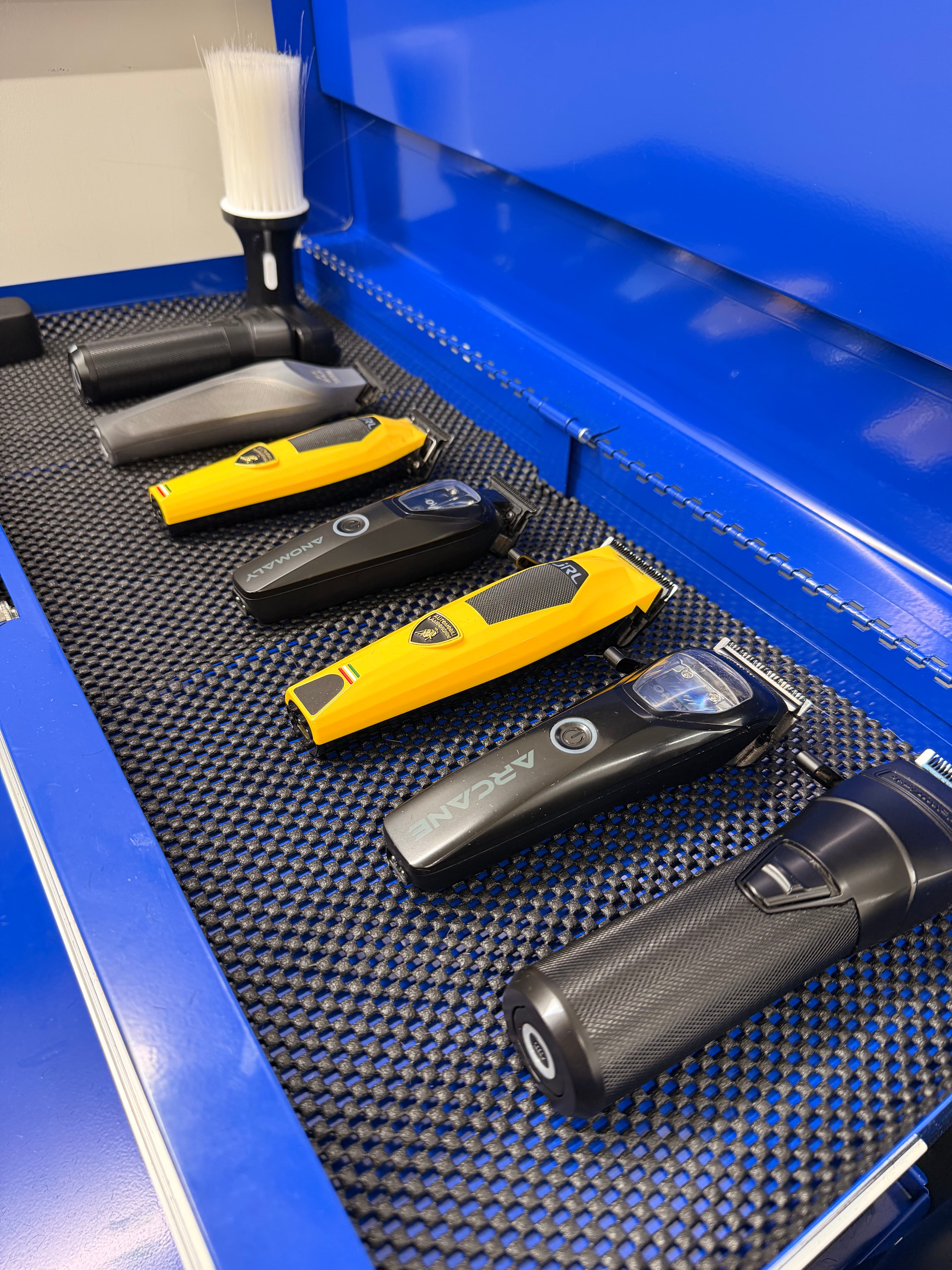 Various professional hair clippers and trimmers neatly organized inside a bright blue metal tool drawer.