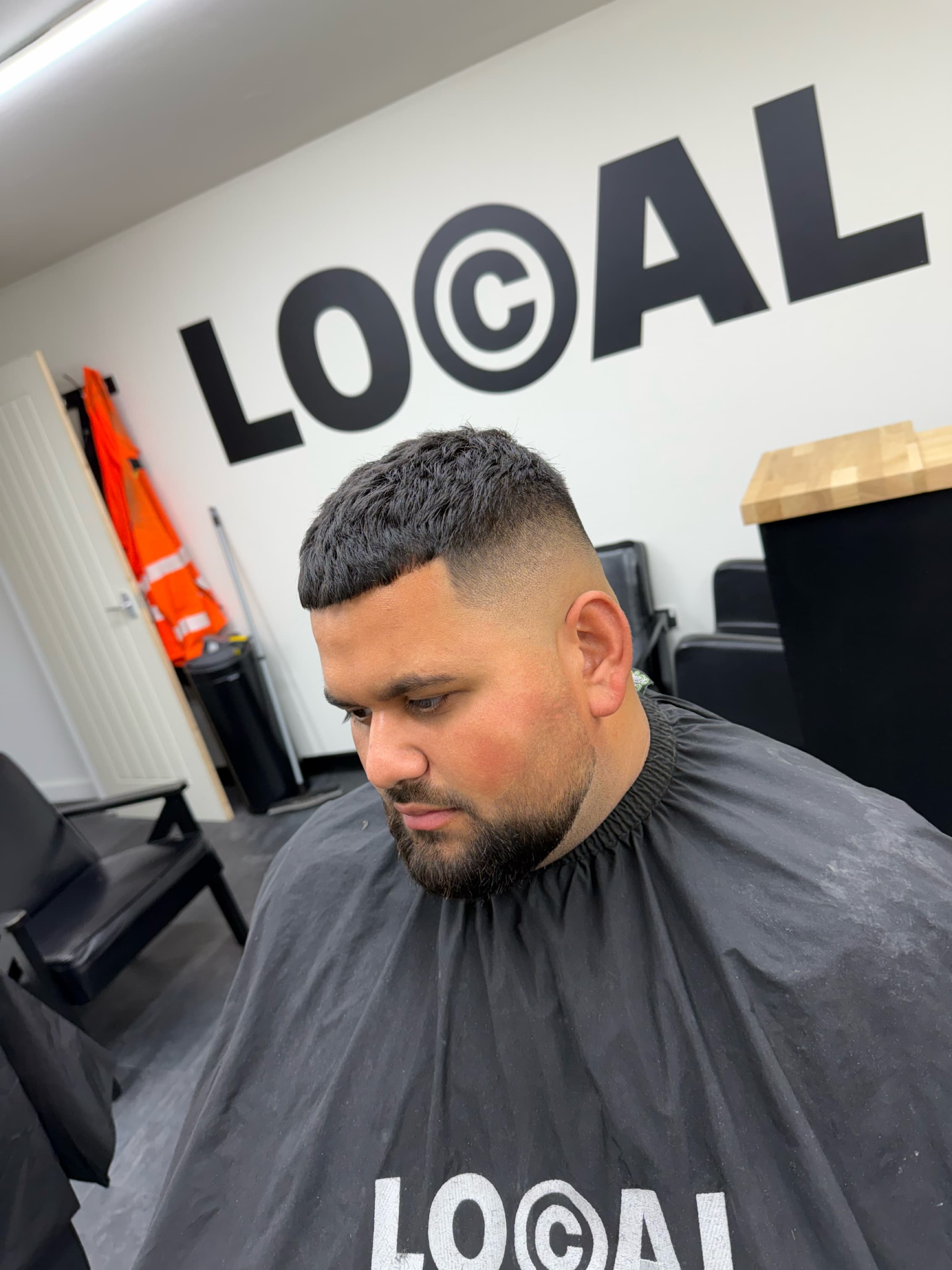 Man with a sharp skin fade and textured crop haircut wearing a black barber cape.