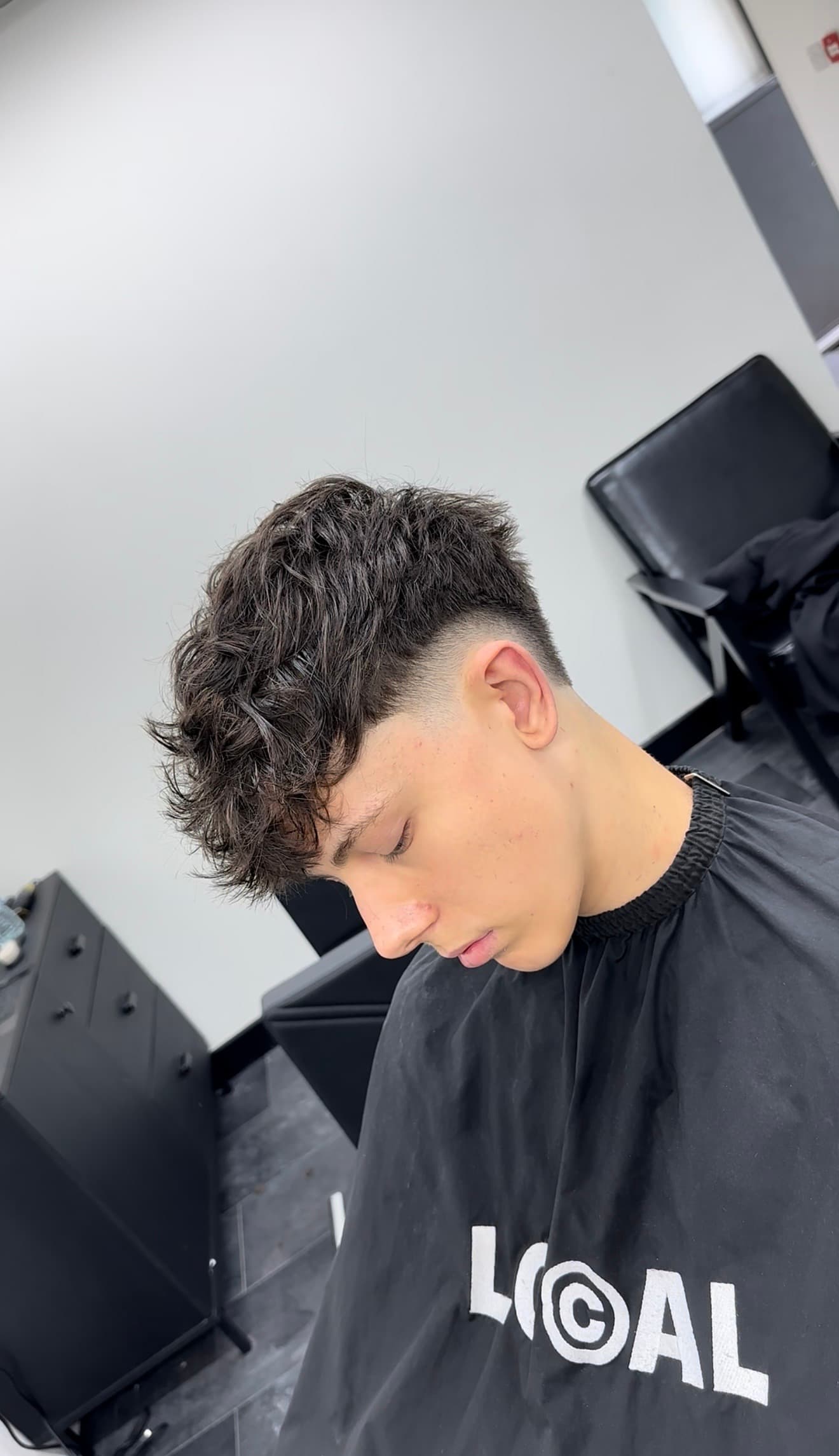 Young man showcasing a textured, messy dark hairstyle with a clean low taper fade.